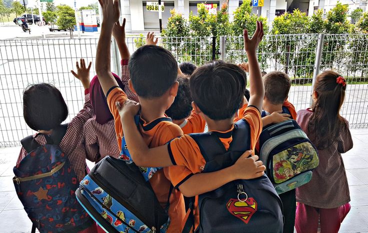 Children in school uniforms and backpacks raising their hands at the school gate on the first day back