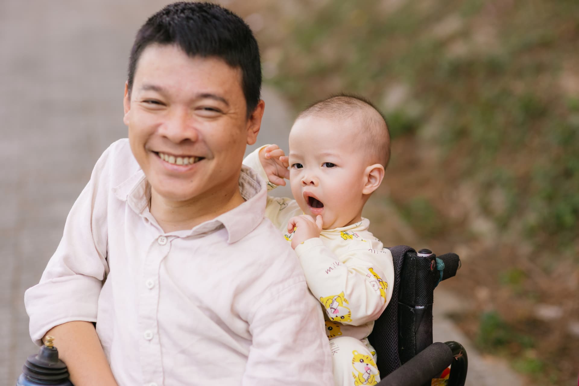 Nguyễn Trung Hậu smiling in his wheelchair, holding his little son Bánh Mì